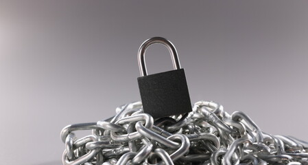 Close-up of solid metal locked padlock on top of tangled silver chain. Set to lock and protect...