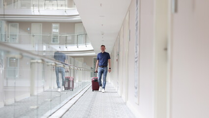 Fototapeta premium Young man with suitcase walking down hotel corridor. Tourism and recreation abroad concept