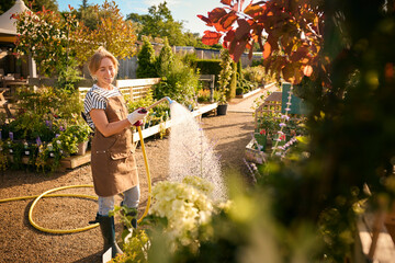 Woman Working Outdoors In Garden Centre Watering Plants