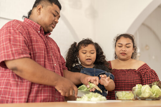 Asian family cooking together at kitchen. The chubby father and mother with girl feel happy in our morning breakfast in a weekend. cooking salad and vegetables.