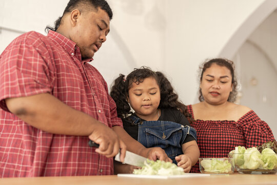 Asian family cooking together at kitchen. The chubby father and mother with girl feel happy in our morning breakfast in a weekend. cooking salad and vegetables.