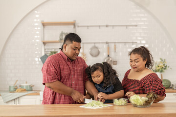 Fototapeta premium Asian family cooking together at kitchen. The chubby father and mother with girl feel happy in our morning breakfast in a weekend. cooking salad and vegetables.
