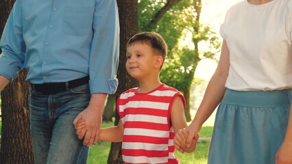 Father mother and son walk holding hands across grass lawn in park at holiday. Cute little kid...