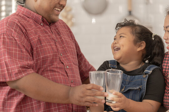 A Chubby Family With A Father Wearing A Prosthetic. They Were Happily Inviting Their Girl To Drink Morning Milk Together In The Kitchen Of Their Home. Breakfast Time Of Asian Dad Mom And Kid People.