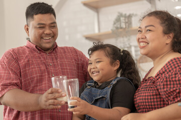 A chubby family with a father wearing a prosthetic. They were happily inviting their girl to drink morning milk together in the kitchen of their home. Breakfast time of Asian dad mom and kid people.