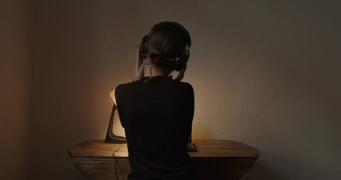 Girl listening with headphones at the table in front of the computer evening