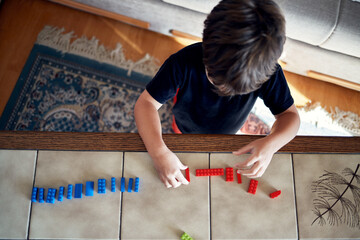 A boy arranges construction kit pieces of the same color in a row