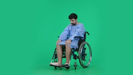 Adult man patient in robe sitting in wheelchair holding hands on his knees looking at legs, sad...