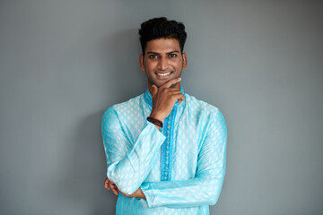 Portrait of confident Indian man in traditional clothes touching chin and smiling at camera