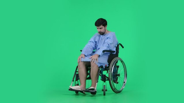 Man in wheelchair looking at his legs, sad depressed expression, shaking head in disbelief. Isolated on chroma key green screen.