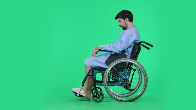 Man in wheelchair looking at his legs, depressed expression, shakes head in disbelief, side view. Isolated on chroma key green screen.