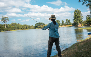 Woman holding fishing rod in her hands into the lake on sunny day.
