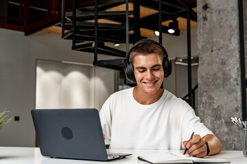 Young man wearing headphones while studying with laptop