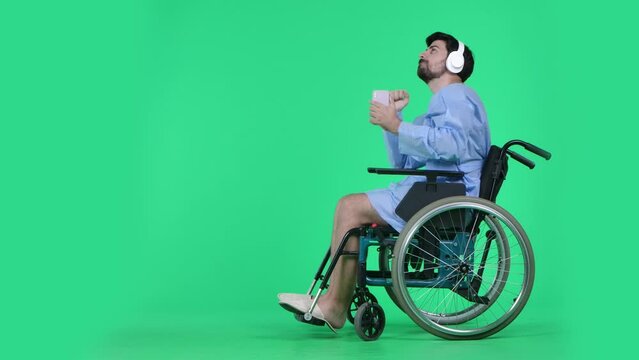Man in wheelchair wearing headphones holding smartphone, listening dancing to music. Isolated on chroma key green screen.