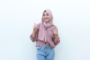 Excited Asian Muslim woman wearing a headscarf gives thumbs up hand gesture of approval, isolated...