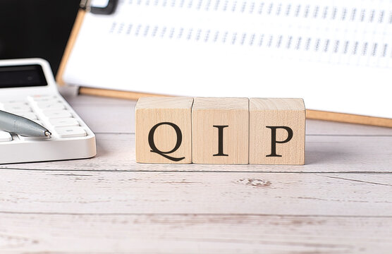 QIP word on a wooden block with clipboard and calcuator