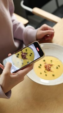 a girl takes a picture of pumpkin cream soup with fried bacon and pumpkin seeds in a bowl