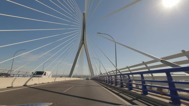 First person view, FPV, from dashcam of car driving across the Constitution of 1812 Bridge, La Pepa, in C&aacute;diz, Andalusia, Spain, Europe. Road trip video in POV, with bright, sunny, clear blue sky