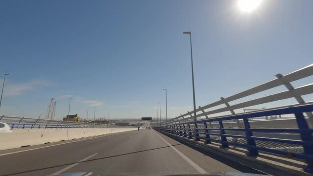First person view, FPV, from dashcam of car driving across the Constitution of 1812 Bridge, La Pepa, in C&aacute;diz, Andalusia, Spain, Europe. Road trip video in POV, with bright, sunny, clear blue sky