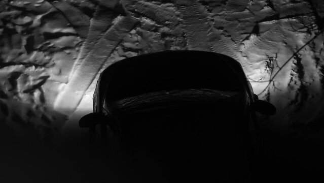 A car at night in winter with its headlights on enters and stops.