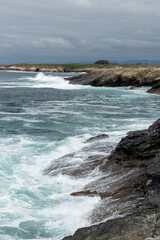 A rocky coastline with turbulent waves crashing, under a cloudy sky, exuding a moody and dramatic atmosphere