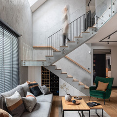 Stylish composition with stairs in living room interior. Grey sofa, green velvet armchair, coffee...