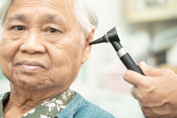 Audiologist or ENT doctor use otoscope checking ear of asian senior woman patient treating hearing...