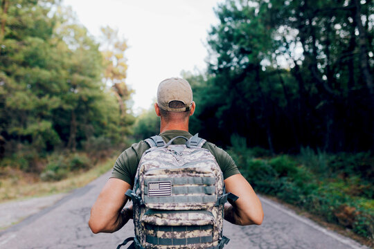 Anonymous middle aged army commando with backpack standing on road against forest