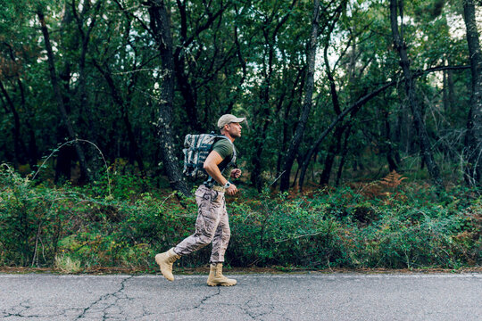 Full body of Soldier training while jogging by plants and trees