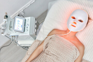Woman lies with led light therapy facial mask in beauty salon