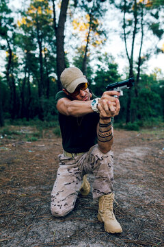 Full body of Military soldier in uniform and cap aiming with gun against forest