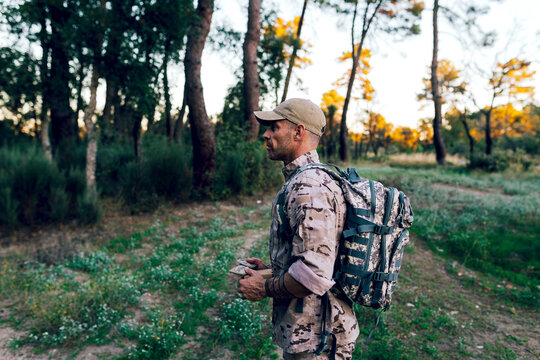 Side view of Army commando with cap and backpack holding box standing in forest