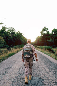 Full body of unrecognizable Mature commando walking on road at sunset