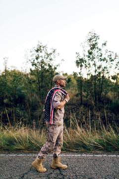 Side view of Mature commando with American flag on shoulder on road under sky at sunset
