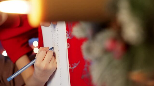 Close-up of children's hands writing a letter to Santa Claus on paper. Celebrating Christmas and waiting for gifts. High quality 4k footage