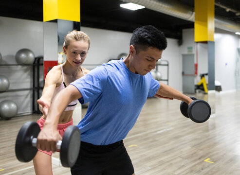 Personal trainer assisting man with dumbbell exercise