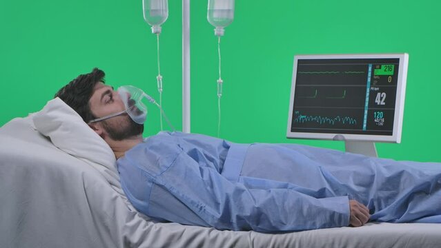 Man in bed with drip, breathing mask and monitor. He breathes fast loses consciousness, heart rate stops. Isolated on chroma key green screen.