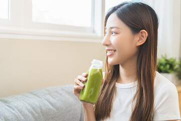 Green detox juice concept, Beautiful smile asian young woman hand holding vegetable smoothie bottle for diet at home. Happy girl drinking healthy meal food for weight loss. Lifestyle, vegan nutrition.