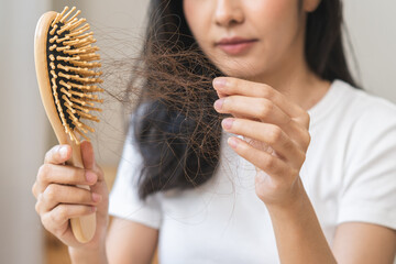 Serious asian young woman holding brush holding comb, hairbrush with fall black hair from scalp after brushing, looking on hand worry about balding. Health care, beauty treatment, hair loss problem. - obrazy, fototapety, plakaty