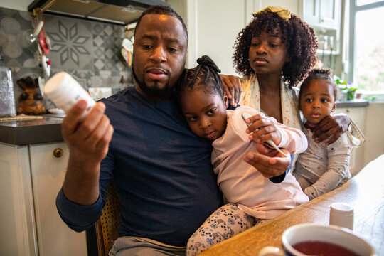 Father Reading Medicine Label with Concerned Mother and Children at Home