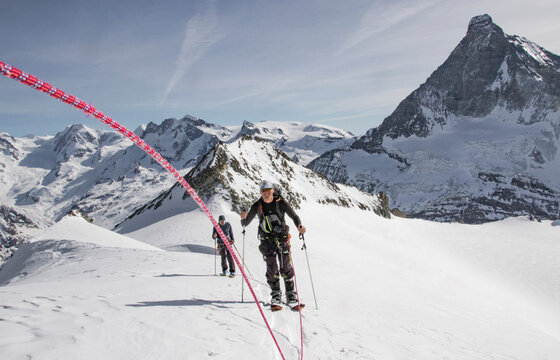 Full body of Happy man skiing on snow-capped mountain with friend on sunny day