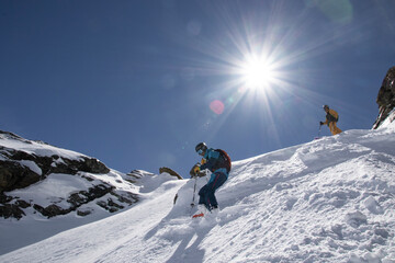 Low angle of Anonymous Tourists in ski suit skiing down on mountain slope on sunny day during vacation at Swiss Alps