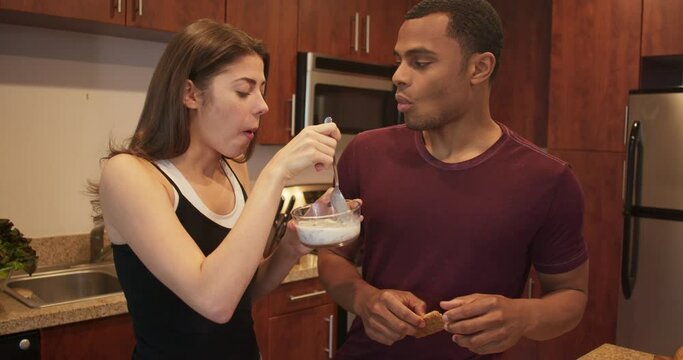 Young millennials in apartment getting ready for the day. African American and Caucasian couple eating cereal for breakfast and talking in the kitchen. 4k slow motion handheld