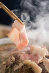 Chopstick holding raw bacon to cook on the grill with smoke. Thai grilled buffet it called Moo ka ta