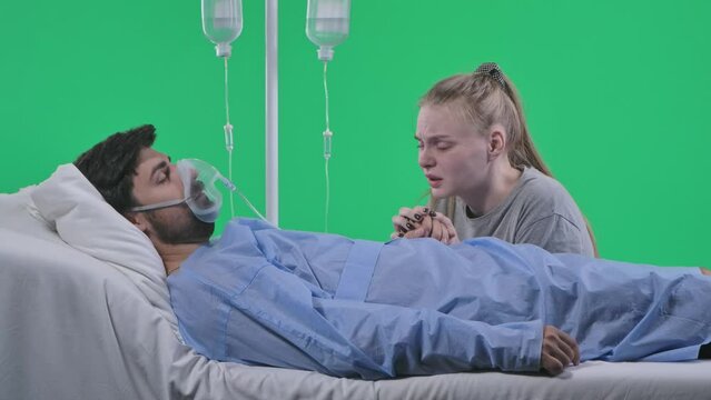 Man in bed with drip, breathing mask and monitor. Girl holding man hand talking, man loses consciousness. Isolated on chroma key green screen.
