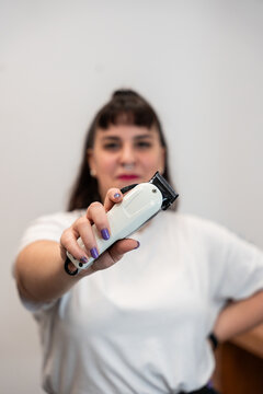 Hairdresser holding electric trimmer against white wall