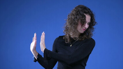 20s Female Expressing Refusal and Disgust with Hand Gesture, woman pushing away with hands sideways on blue background