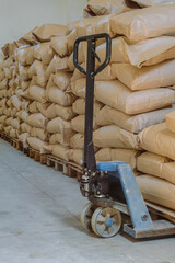 Hydraulic lifter carriage - hand pallet truck. Filled kraft paper bags on wooden pallets in warehouse room of an industrial building.