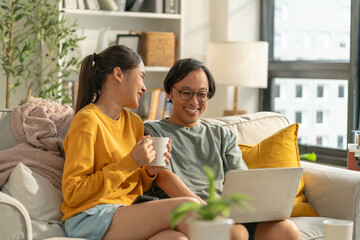 Asian couple family lifestyle,technology concept.Happy young Asian couple using cellphone,watch movie online,browsing internet,chatting online,checking new mobile application,relaxing on sofa at home
 - obrazy, fototapety, plakaty