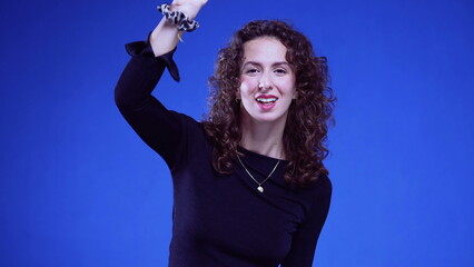 Happy woman greeting to camera with hand gesture standing on blue background. 20s Person saying...